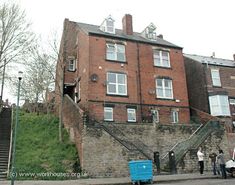 an old brick building on the corner of a street with people walking around it and cars parked in front