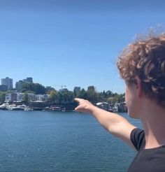 a person pointing at something in the distance on a lake with boats and buildings in the background