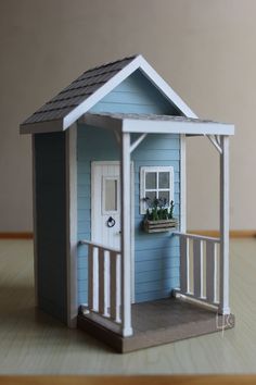 a small doll house with a porch and flower box on the door step, sitting on top of a wooden table