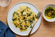 a white plate topped with ravioli and spinach next to a bowl of pesto