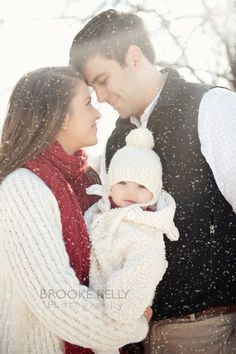 a man and woman standing next to each other holding a baby in their arms while it is snowing