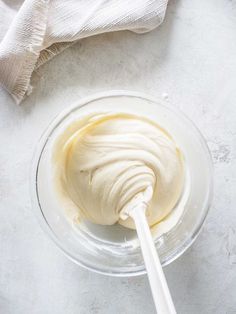 a glass bowl filled with whipped cream on top of a white tablecloth next to a spoon