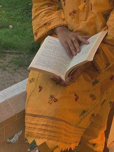 a person sitting down holding an open book in their hands and reading it on the ground