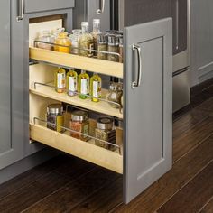 a pull out spice rack in the middle of a kitchen with gray cabinets and wood flooring