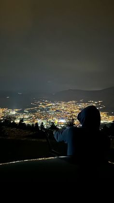 a person sitting on top of a hill looking at the city lights in the distance