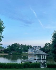 a gazebo sits in the middle of a lake surrounded by trees and bushes with a house in the background