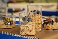 three clear cups filled with dirt and toys on top of a table covered in checkered cloth