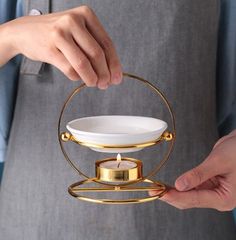 a person holding a tea light holder with a candle in it's center and two hands on the other side