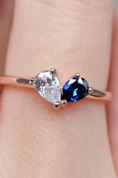 a woman's hand holding an engagement ring with two pear shaped blue and white diamonds