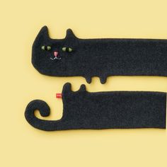 two black cats made out of felt sitting next to each other on a yellow surface