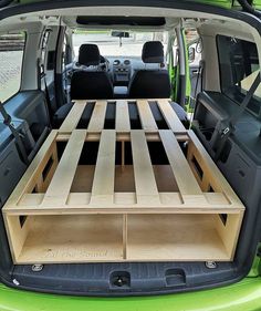 the back end of a green van with an open trunk and two wooden shelves in it