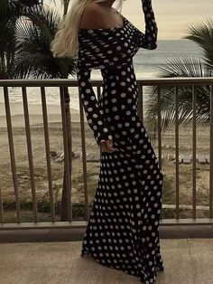 a woman in a black and white polka dot dress standing on a balcony overlooking the ocean