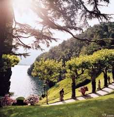 the sun shines brightly through the trees and over the water as people walk along a path