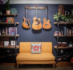 guitars are hanging on the wall above a couch and bookshelf in a living room