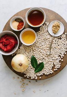 an assortment of foods are arranged on a wooden platter with spoons and spices