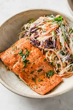 two salmons and coleslaw in a bowl on a white counter top with a fork