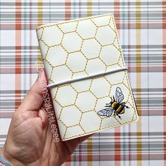 a hand holding a small white and yellow notebook with a bee on the front cover