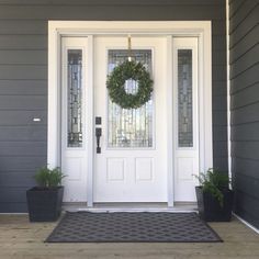 a front door with a wreath on it and two planters in the foreground