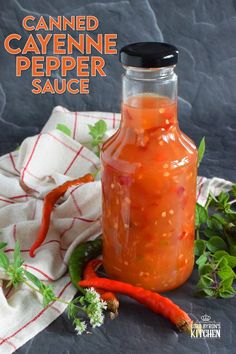 a glass jar filled with canned cayenne pepper sauce next to some fresh vegetables