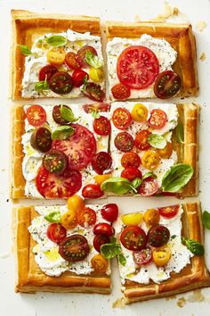 four square pieces of bread with tomatoes, mozzarella and basil on them sitting on a white surface