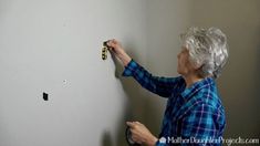 an older woman is working on the wall with screws and magnets attached to it