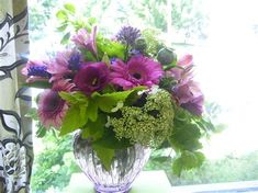 a vase filled with purple and green flowers sitting on top of a window sill