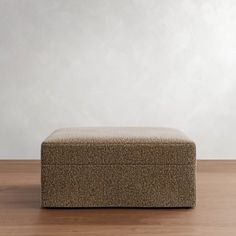 a brown ottoman sitting on top of a hard wood floor next to a white wall