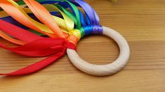 a rainbow colored wooden ring with ribbon on it sitting on a table next to flowers