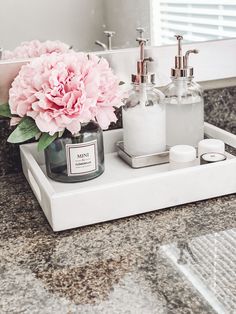 a pink flower sitting on top of a bathroom counter next to two soap dispensers