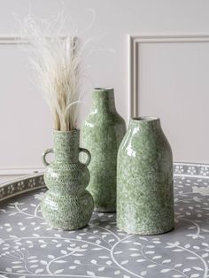 two green vases sitting on top of a table next to a plant in a vase