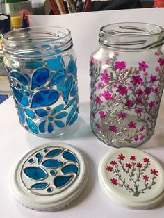 three glass jars sitting on top of a table next to each other with flowers painted on them