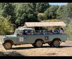 an old pick up truck with people in the back driving down a dirt road next to trees