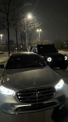 two cars are parked on the side of the road at night, one is silver and the other is black