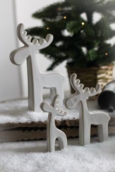 two white reindeer figurines sitting next to a small christmas tree in the snow