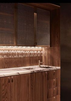 a kitchen with wooden cabinets and marble counter tops, wine glasses hanging on the wall