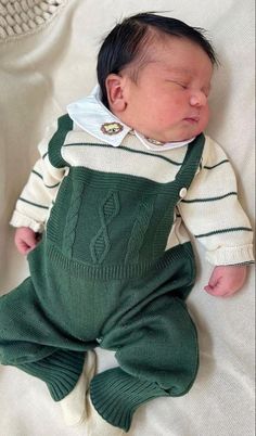 a baby laying on top of a bed wearing green overalls and a white shirt