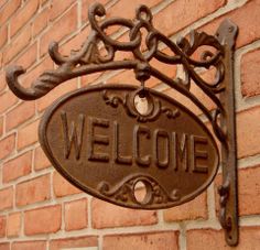 a welcome sign on the side of a brick building with an iron frame hanging from it's corner