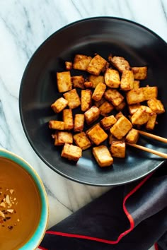 tofu sticks in a black bowl with brown sauce and garnish on the side