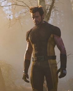 the wolverine man is standing in front of some trees and looking off into the distance