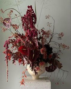 a white vase filled with lots of flowers on top of a table next to a wall