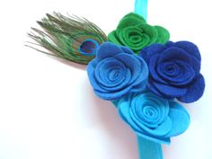 "Peacock Felt Headband. Four felt flower roses in Peacock Blue, Green, Cerulean Blue and Royal Blue, attached to a shimmery turquoise soft elastic headband, with a Peacock feather. The roses are set on felt on the headband for comfort and softness. The roses measure 2 inches across. Total measurement of Peacock blooms are 5 inches across the headband. Height of the Peacock bouquet is 4 inches. Perfect for; 1st birthdays, birthday photos, fantasy photos, birthday gifts, tea parties, as a whimsica Peacock Bouquet, Kids Costumes Halloween, Peacock Headband, Hair Accessories Kids, Felt Headband, Cerulean Blue, Elastic Headband, 1st Birthdays, Headband Baby