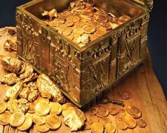 a wooden table topped with lots of gold coins and an open chest filled with them