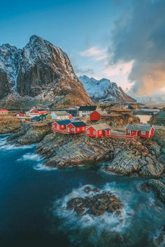 an aerial view of some red houses on the coast with mountains in the background and blue water