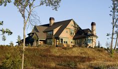 a large house sitting on top of a grass covered hill next to trees and bushes