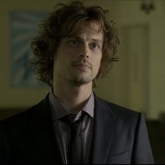 a man with curly hair wearing a suit and tie looking at the camera while standing in a room