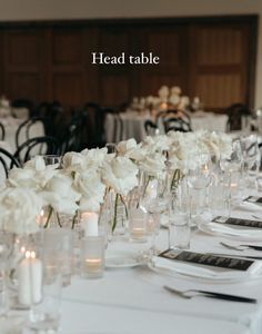 there is a long table with white flowers and place settings on it, along with silverware