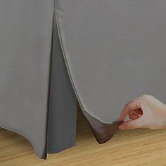 a person is pulling up the side of a bed with a gray sheet on it