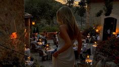 a woman in a white dress is standing outside at night with candles lit on the ground