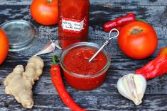 a jar of ketchup next to some vegetables and garlic on a wooden table