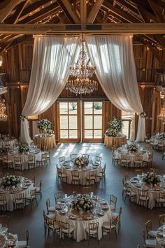 the inside of a barn with tables, chairs and chandeliers set up for an event